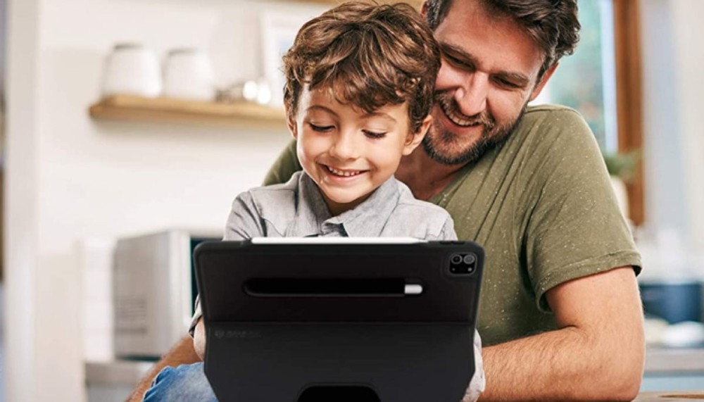 a young boy and his father looking at the screen of an iPad with a sturdy black case on it supporting it