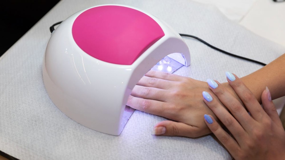 A woman places her fingers under a nail light on top of a towel.