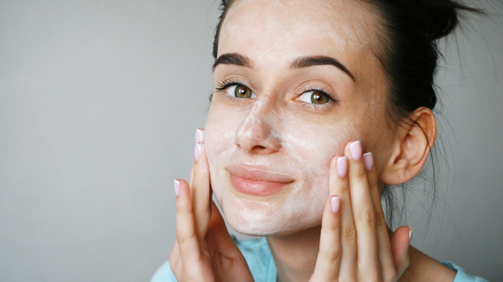 A young woman cleans her face with an exfoliating product