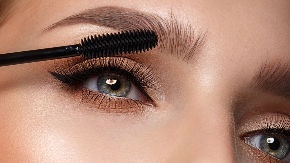 A woman applies mascara to her eyelashes.