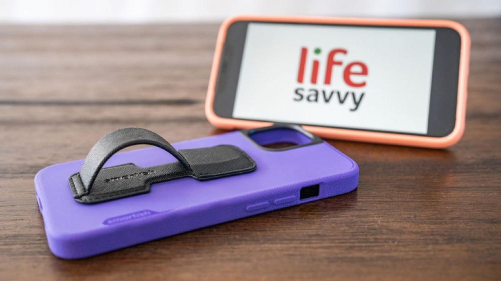 A purple phone case with a black phone ring on it sitting next to a smartphone displaying the Lifesavvy logo