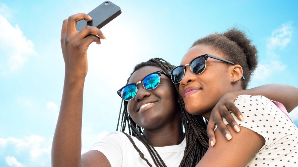 Two women taking a selfie outdoors with blue sky behind them.