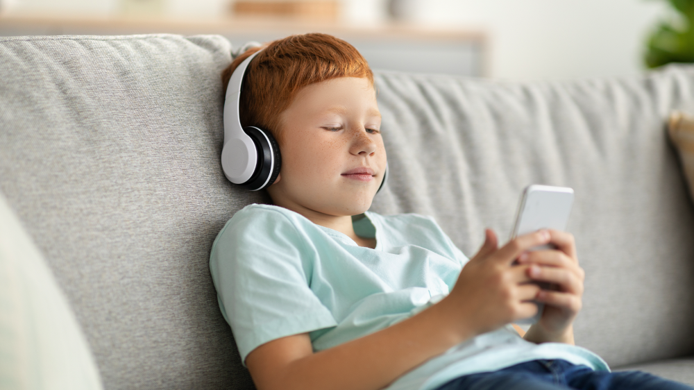 A child playing on a phone while wearing headphones.